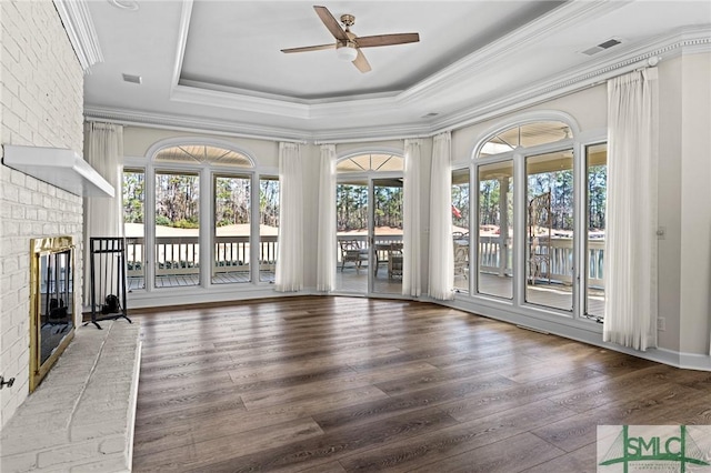 unfurnished living room featuring a wealth of natural light, a raised ceiling, a fireplace, and wood finished floors