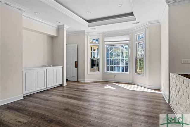 interior space with baseboards, wood finished floors, a raised ceiling, and crown molding