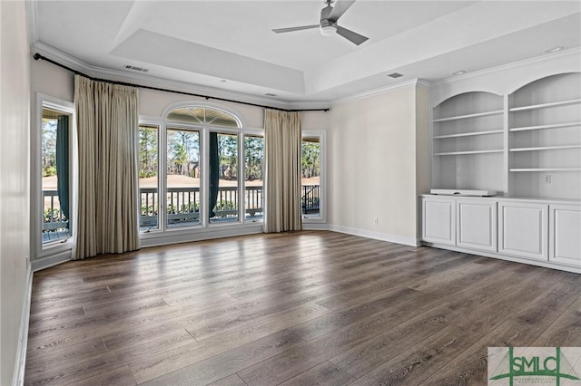 unfurnished living room featuring plenty of natural light, built in shelves, and a tray ceiling