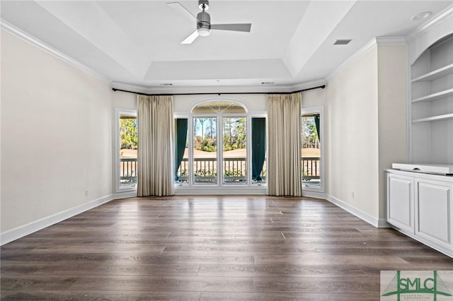 unfurnished room with built in shelves, a tray ceiling, a healthy amount of sunlight, and wood finished floors