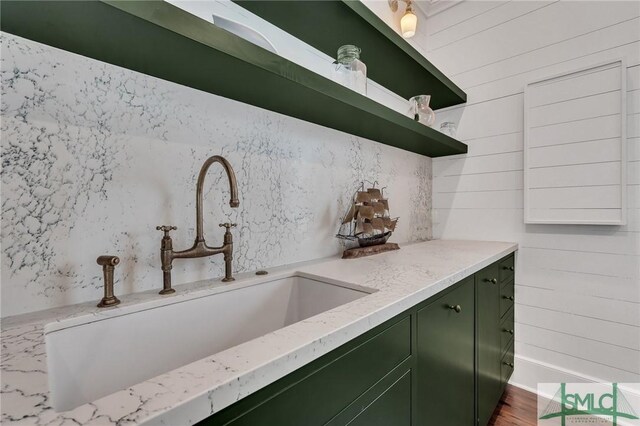 kitchen featuring dark wood-style flooring, open shelves, green cabinets, a sink, and light stone countertops
