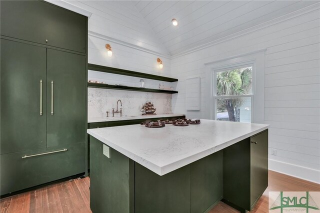 kitchen featuring lofted ceiling, green cabinets, wood finished floors, open shelves, and a sink
