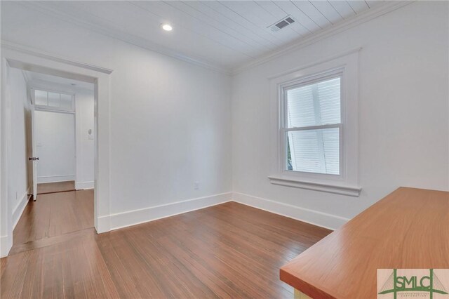 empty room featuring baseboards, visible vents, wood finished floors, and ornamental molding