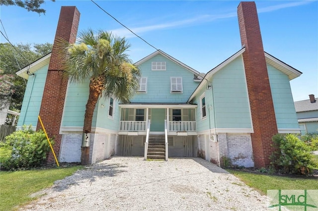view of front of property featuring gravel driveway, brick siding, a chimney, a porch, and stairs