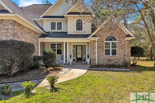 traditional-style house with brick siding, roof with shingles, covered porch, a front lawn, and stucco siding