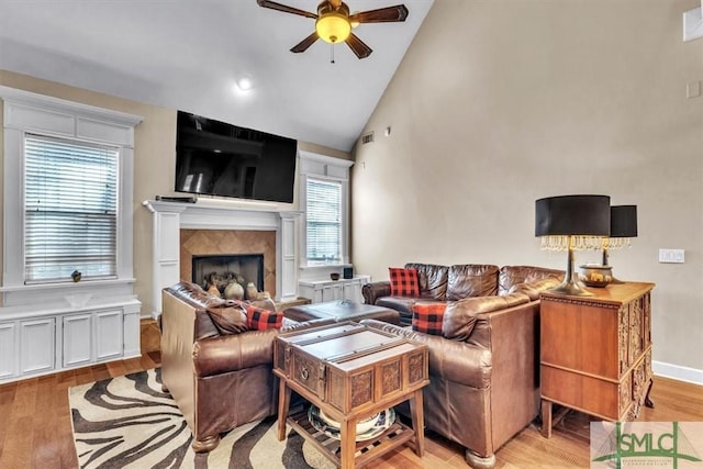 living room with light wood finished floors, baseboards, a ceiling fan, high vaulted ceiling, and a high end fireplace