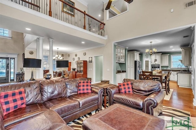 living area featuring ornamental molding, light wood-type flooring, visible vents, and an inviting chandelier