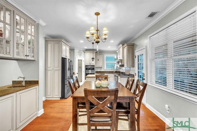 dining space featuring a notable chandelier, visible vents, light wood-style flooring, ornamental molding, and baseboards