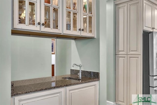 kitchen featuring dark stone countertops, glass insert cabinets, a sink, and freestanding refrigerator