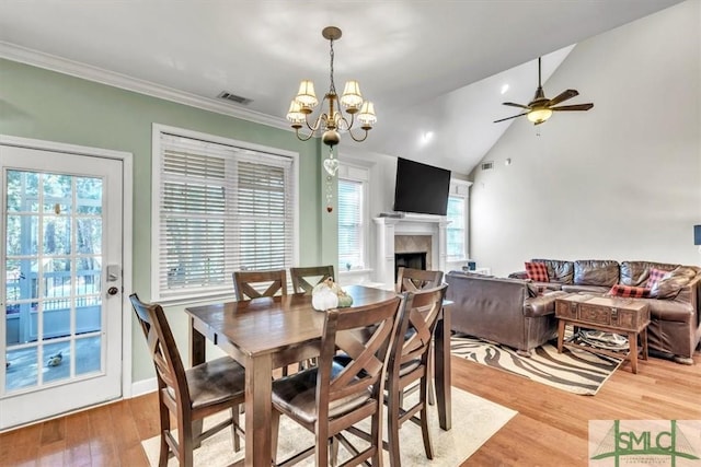 dining room with a fireplace, crown molding, lofted ceiling, visible vents, and light wood-style floors