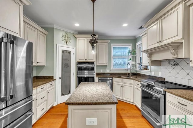 kitchen with light wood-style flooring, appliances with stainless steel finishes, a sink, and ornamental molding