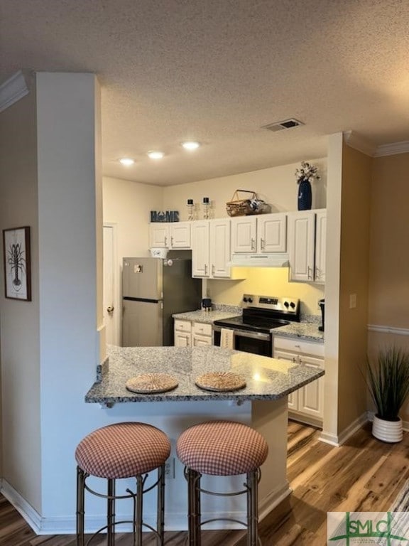 kitchen with a breakfast bar area, under cabinet range hood, stainless steel appliances, wood finished floors, and visible vents