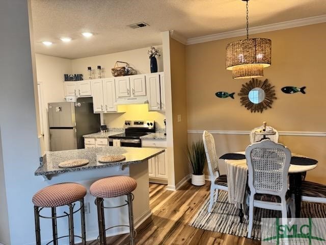 kitchen with appliances with stainless steel finishes, a kitchen breakfast bar, wood finished floors, under cabinet range hood, and pendant lighting