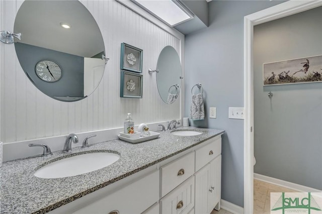 full bath featuring double vanity, a sink, and baseboards