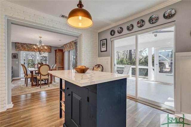 kitchen with wainscoting, a kitchen breakfast bar, crown molding, light wood-type flooring, and pendant lighting