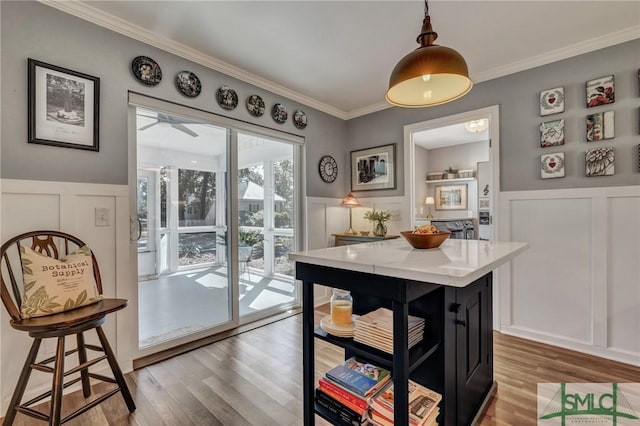 kitchen featuring a wainscoted wall, light countertops, ornamental molding, and wood finished floors