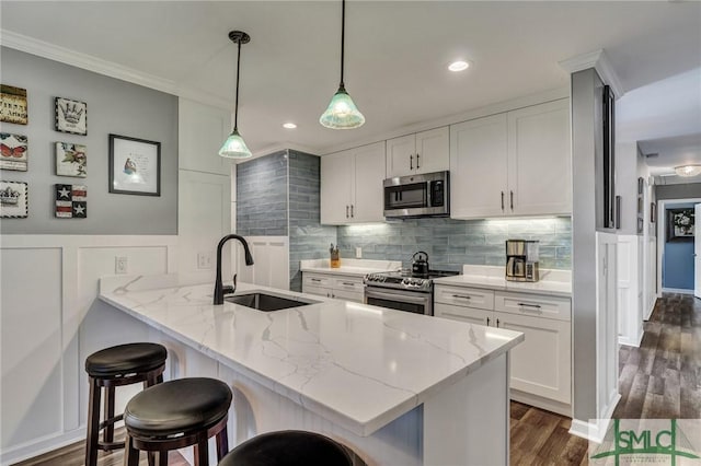 kitchen with a peninsula, a sink, appliances with stainless steel finishes, decorative backsplash, and a kitchen bar