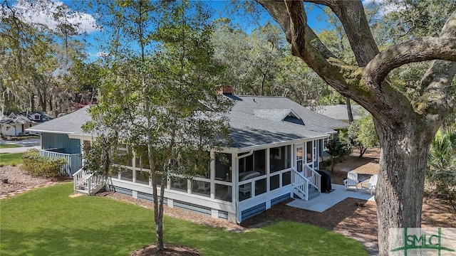 back of house with a yard, a chimney, a patio, a shingled roof, and a sunroom