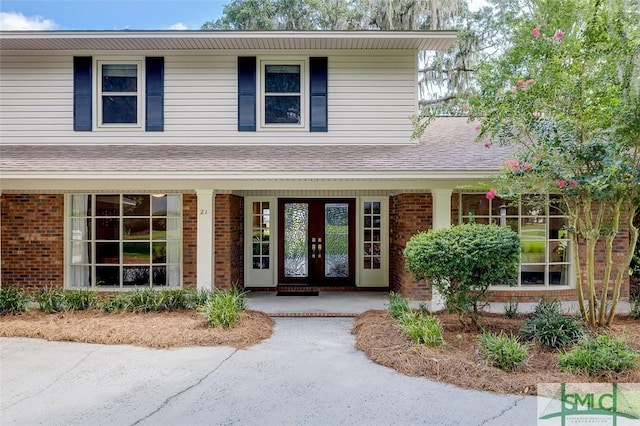 property entrance featuring a porch, brick siding, and roof with shingles