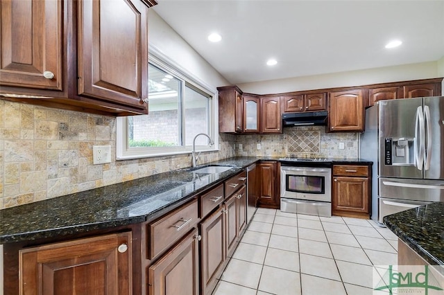 kitchen featuring light tile patterned floors, under cabinet range hood, stainless steel appliances, a sink, and dark stone countertops