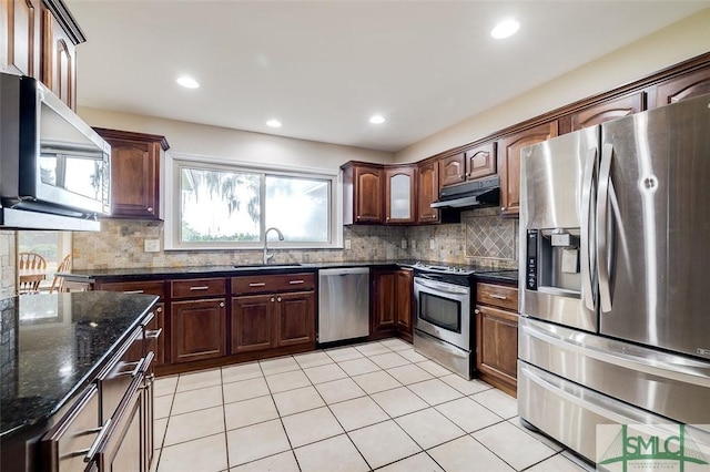 kitchen with decorative backsplash, appliances with stainless steel finishes, a sink, dark stone countertops, and under cabinet range hood