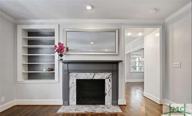 unfurnished living room featuring built in shelves, a premium fireplace, ornamental molding, wood finished floors, and baseboards