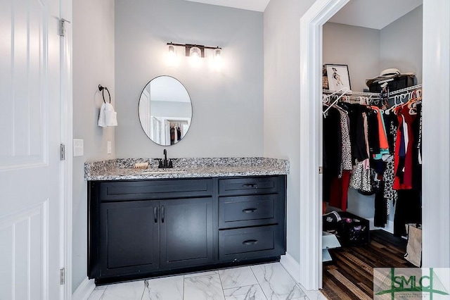 bathroom featuring marble finish floor, a spacious closet, vanity, and baseboards