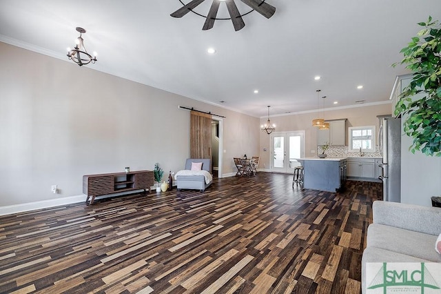 unfurnished living room featuring a barn door, baseboards, and crown molding