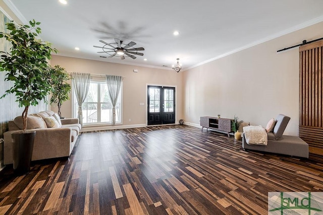 living area featuring a barn door, ornamental molding, dark wood finished floors, and baseboards