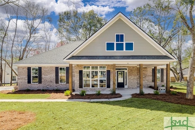 view of front of house featuring a shingled roof, a front yard, and brick siding