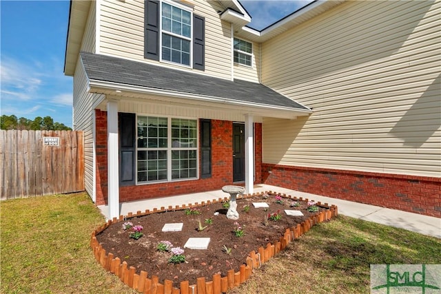 view of exterior entry featuring a porch, a yard, brick siding, and fence