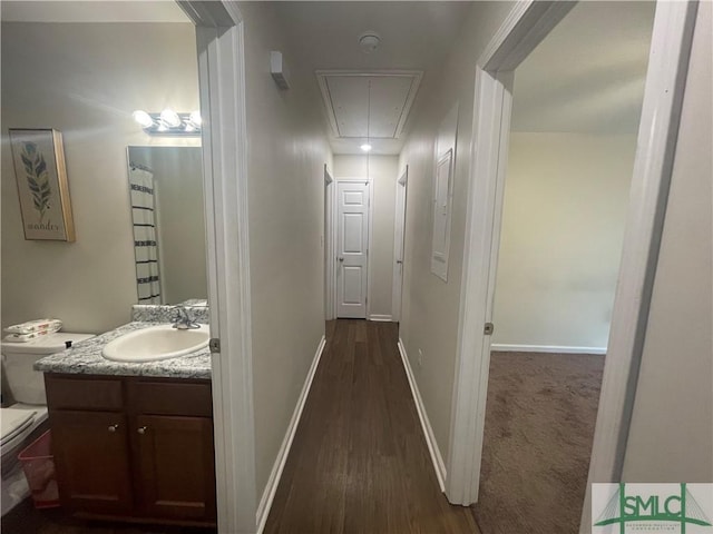 corridor featuring attic access, baseboards, dark wood finished floors, and a sink