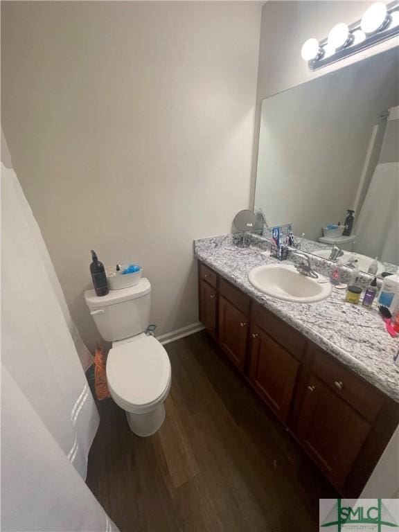 bathroom featuring toilet, baseboards, wood finished floors, and vanity