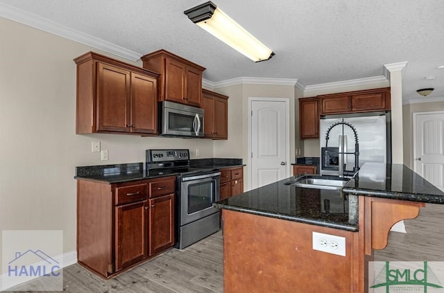 kitchen with light wood finished floors, appliances with stainless steel finishes, dark stone countertops, a kitchen island with sink, and crown molding