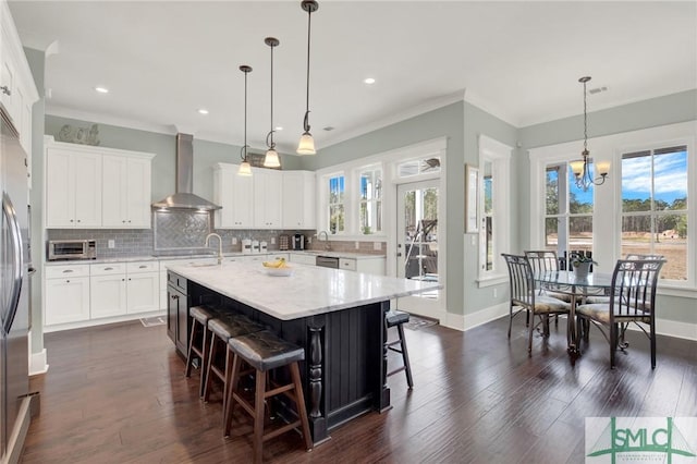 kitchen featuring dark wood-style floors, a center island with sink, tasteful backsplash, wall chimney range hood, and a kitchen bar