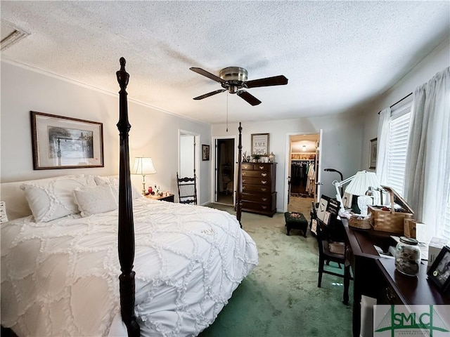 bedroom featuring a textured ceiling, ceiling fan, light colored carpet, a walk in closet, and crown molding