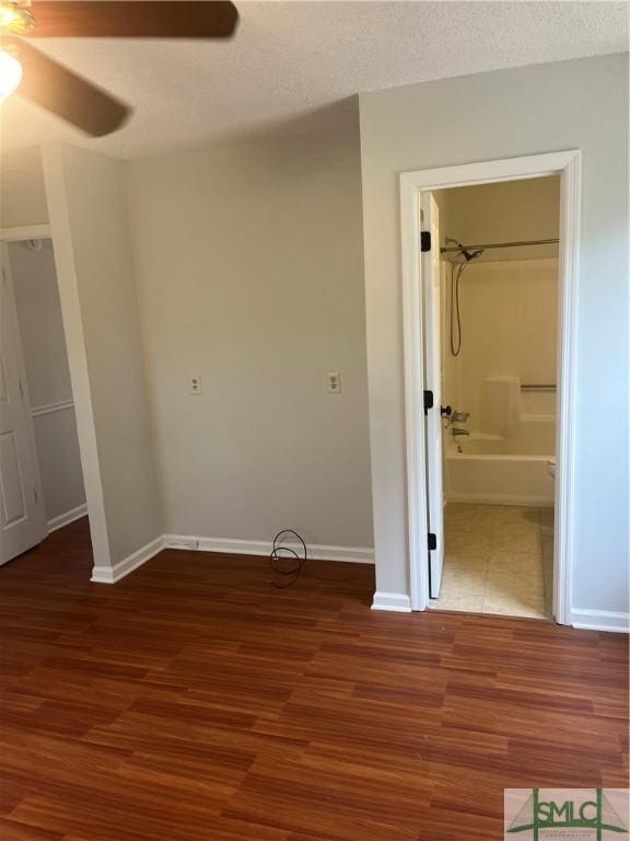 unfurnished bedroom featuring connected bathroom, a textured ceiling, baseboards, and wood finished floors