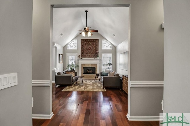 living area featuring baseboards, a tiled fireplace, ceiling fan, dark wood-type flooring, and high vaulted ceiling