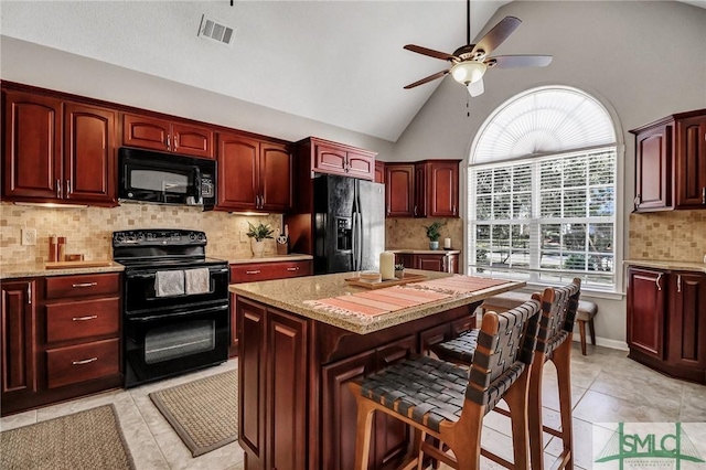 kitchen featuring reddish brown cabinets, a kitchen breakfast bar, visible vents, and black appliances