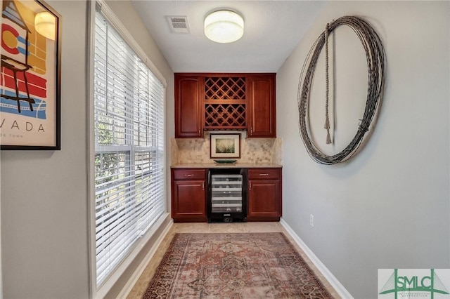 bar featuring wine cooler, visible vents, backsplash, a bar, and baseboards