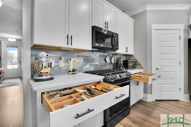 kitchen with black gas range, light wood finished floors, white cabinets, decorative backsplash, and light countertops