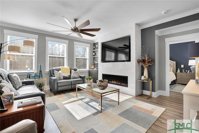 living area with light wood finished floors, a fireplace, baseboards, and crown molding