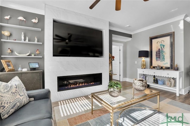 living area featuring built in shelves, crown molding, a fireplace, ceiling fan, and wood finished floors