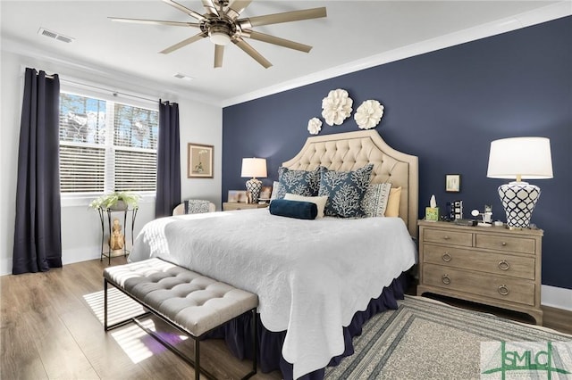 bedroom with visible vents, crown molding, baseboards, and wood finished floors