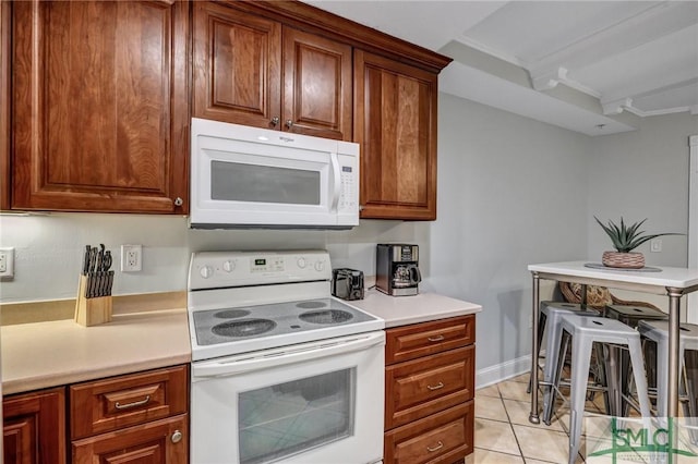 kitchen featuring white appliances, light tile patterned floors, brown cabinetry, baseboards, and light countertops