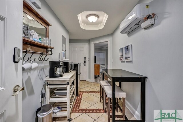 kitchen with light tile patterned floors, an AC wall unit, a raised ceiling, and baseboards