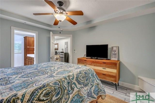 bedroom featuring ceiling fan, a tray ceiling, baseboards, and wood finished floors