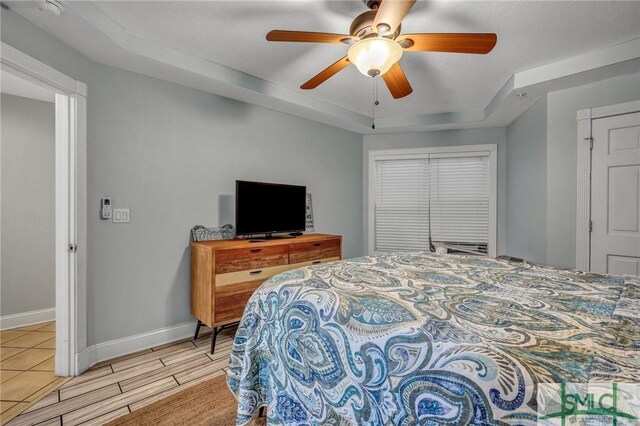 bedroom with light wood finished floors, ceiling fan, baseboards, and a tray ceiling