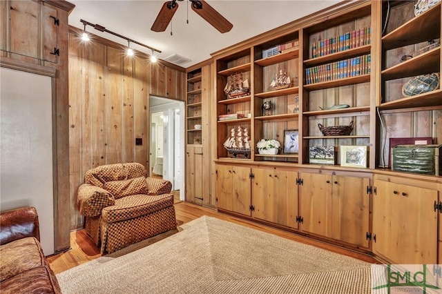 sitting room featuring ceiling fan, light wood-type flooring, rail lighting, and wooden walls