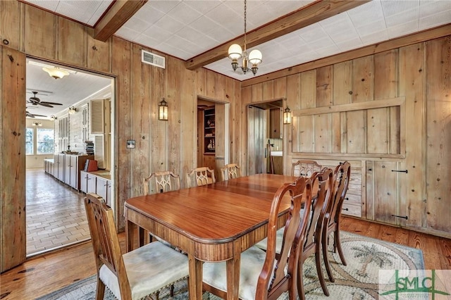 dining area featuring wooden walls, visible vents, beamed ceiling, and wood finished floors